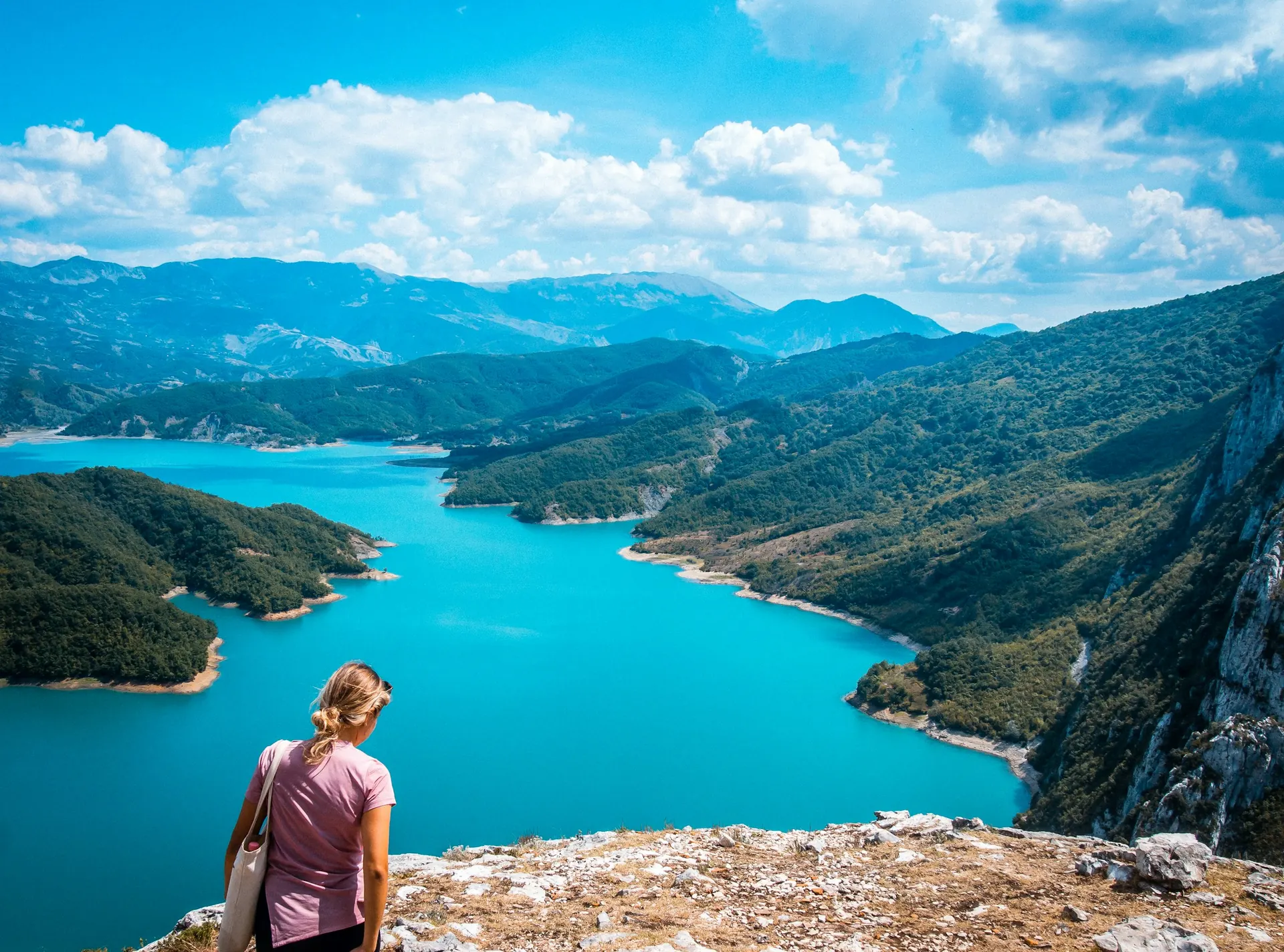 A hiker looking down on the turquoise water of Bovilla Lake from the Gamti trail